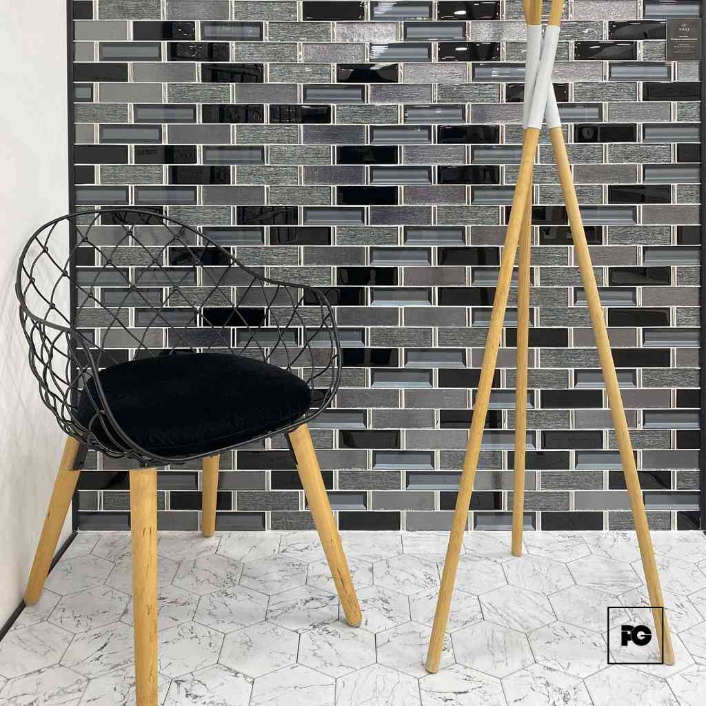 Modern interior corner with a black wire chair and a tall wooden tripod lamp against a gray glass-tile wall and white tiled floor.